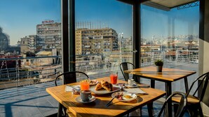A breakfast table with croissants, eggs, and juice, overlooking a cityscape with buildings and a view of the sea. - Sweet Sleep (Naples)
