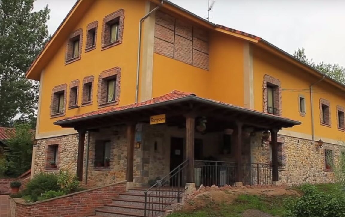 A yellow building with a stone base, multiple windows, and a porch with steps leading up to it.