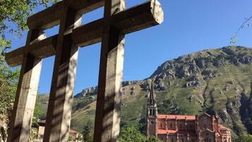 A stone cross structure with a view of a mountainous landscape and a red-roofed building in the background.