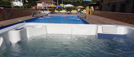 A swimming pool with a hot tub in the foreground, lounge chairs, and umbrellas in the background.