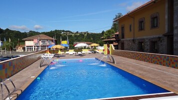 Piscina com deck revestido, espreguiçadeiras e guarda-sóis.