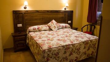 Una cama bien tendida con ropa de cama floral, dos lámparas de noche, una mesita de noche y una silla.