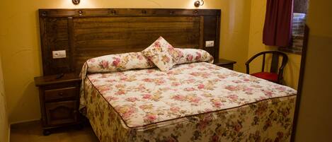 A neatly made bed with floral bedding, two bedside lamps, a nightstand, and a chair.