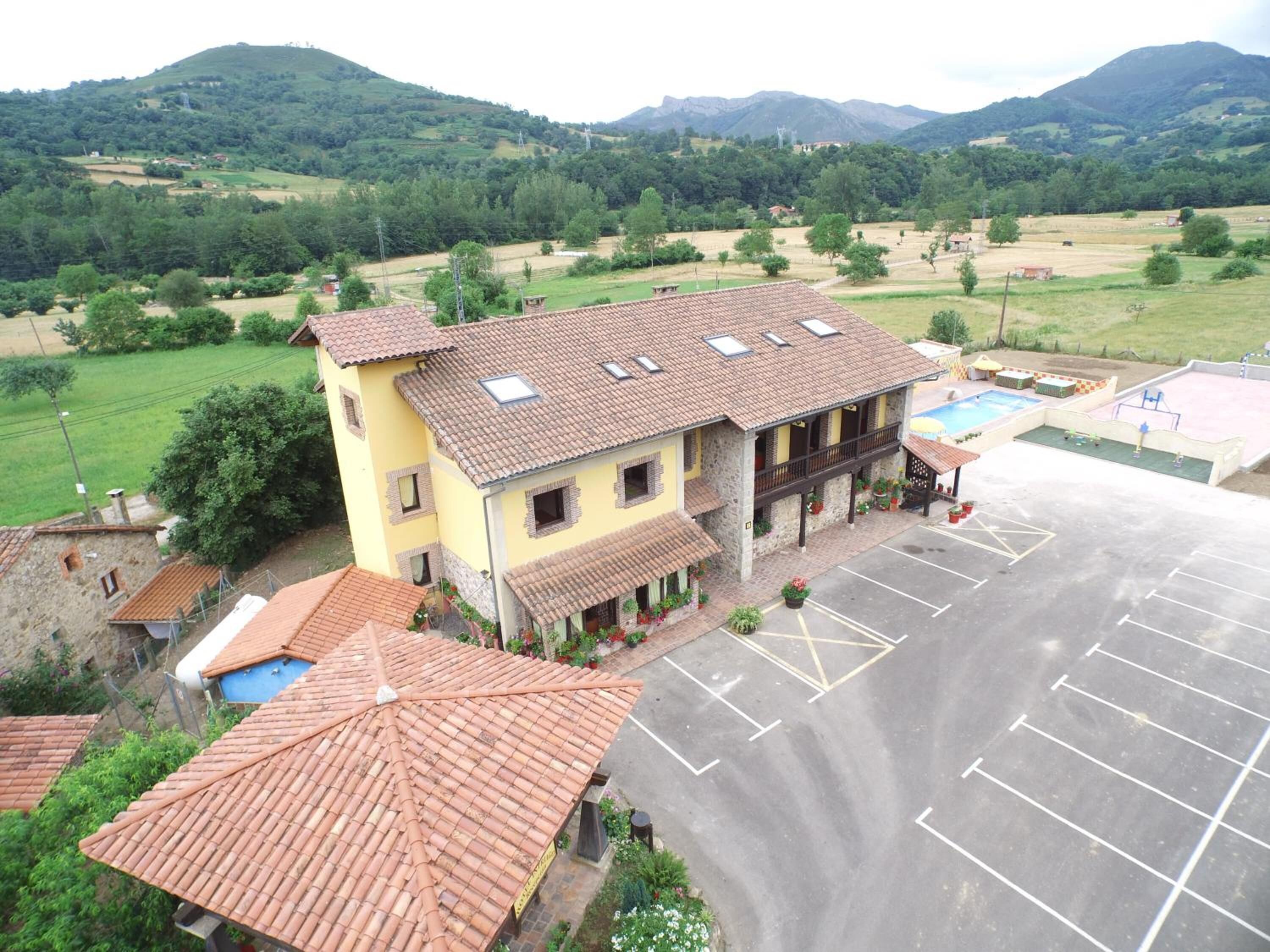 A two-story building with a tiled roof, a parking lot, and a view of green hills in the background.