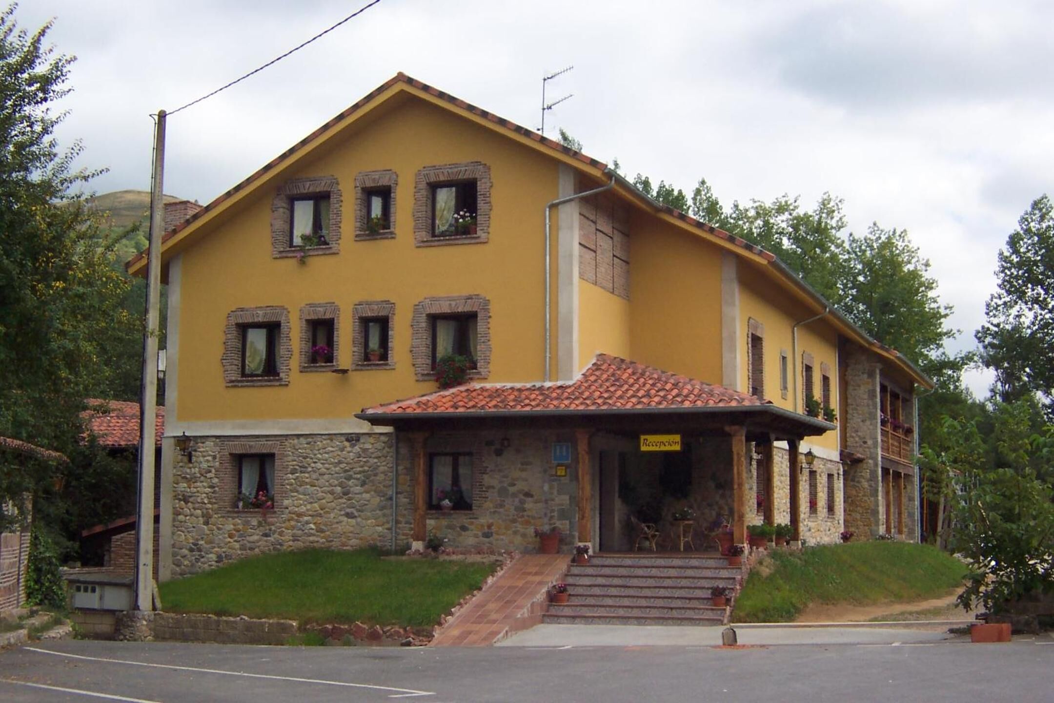 A two-story building with a yellow facade, stone lower section, and a tiled roof.