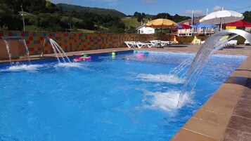Piscina com jatos de água, rodeada por um muro revestido e área de estar ao ar livre.