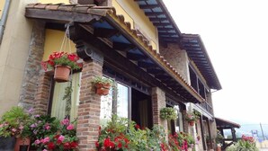 Un edificio con fachada de ladrillo, varias ventanas adornadas con macetas colgantes y una estructura de balcón de madera.
