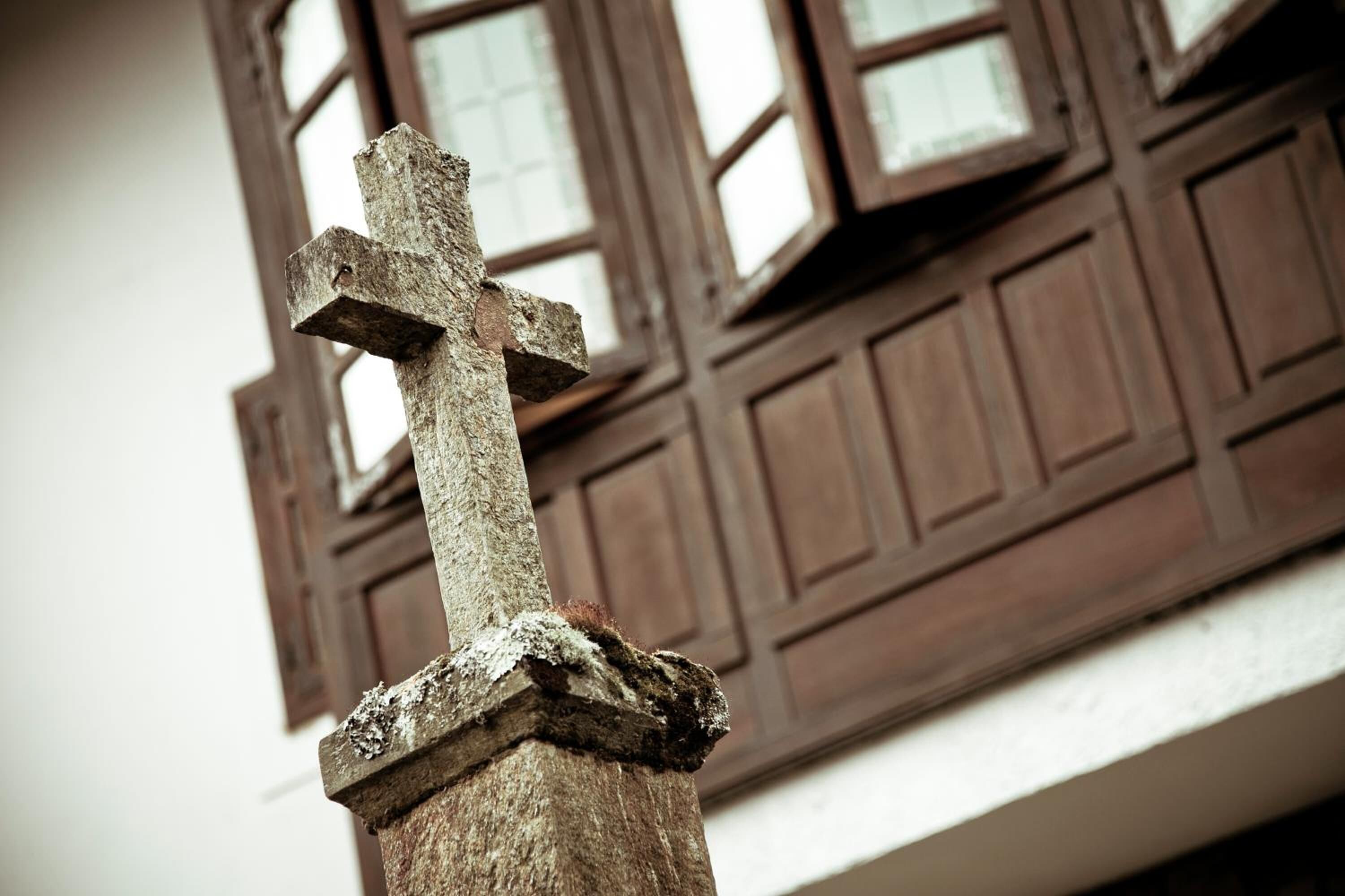 Ein verwittertes hölzernes Kreuz, befestigt an einem steinernen Pfeiler.