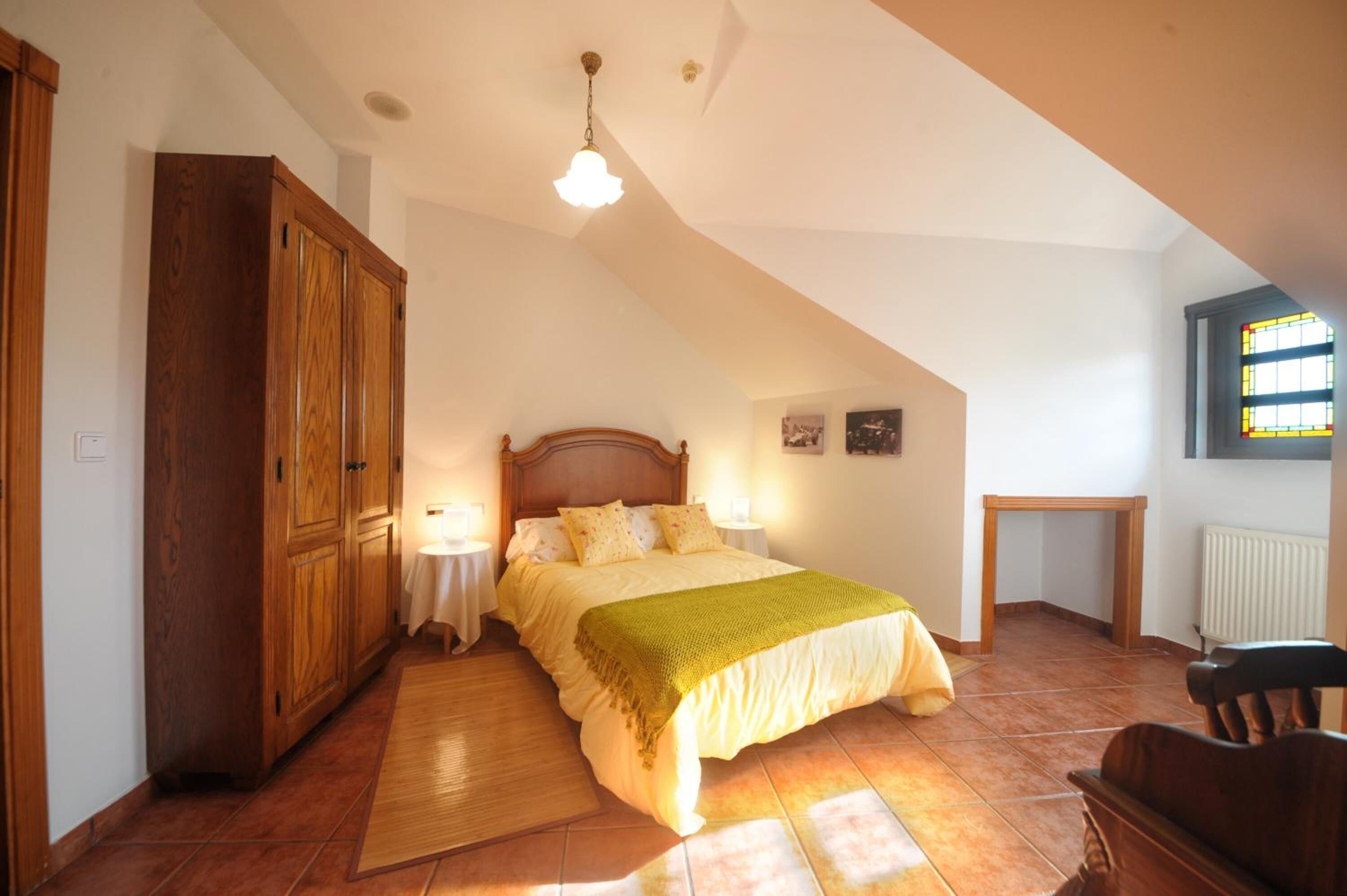 A bedroom with a large bed, wooden wardrobe, and a small table by the window.