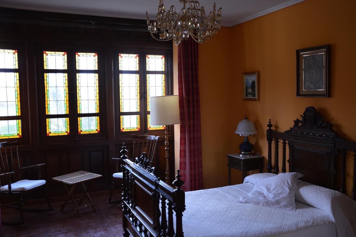 A room with a bed, a chandelier, a table, chairs, and stained glass windows.