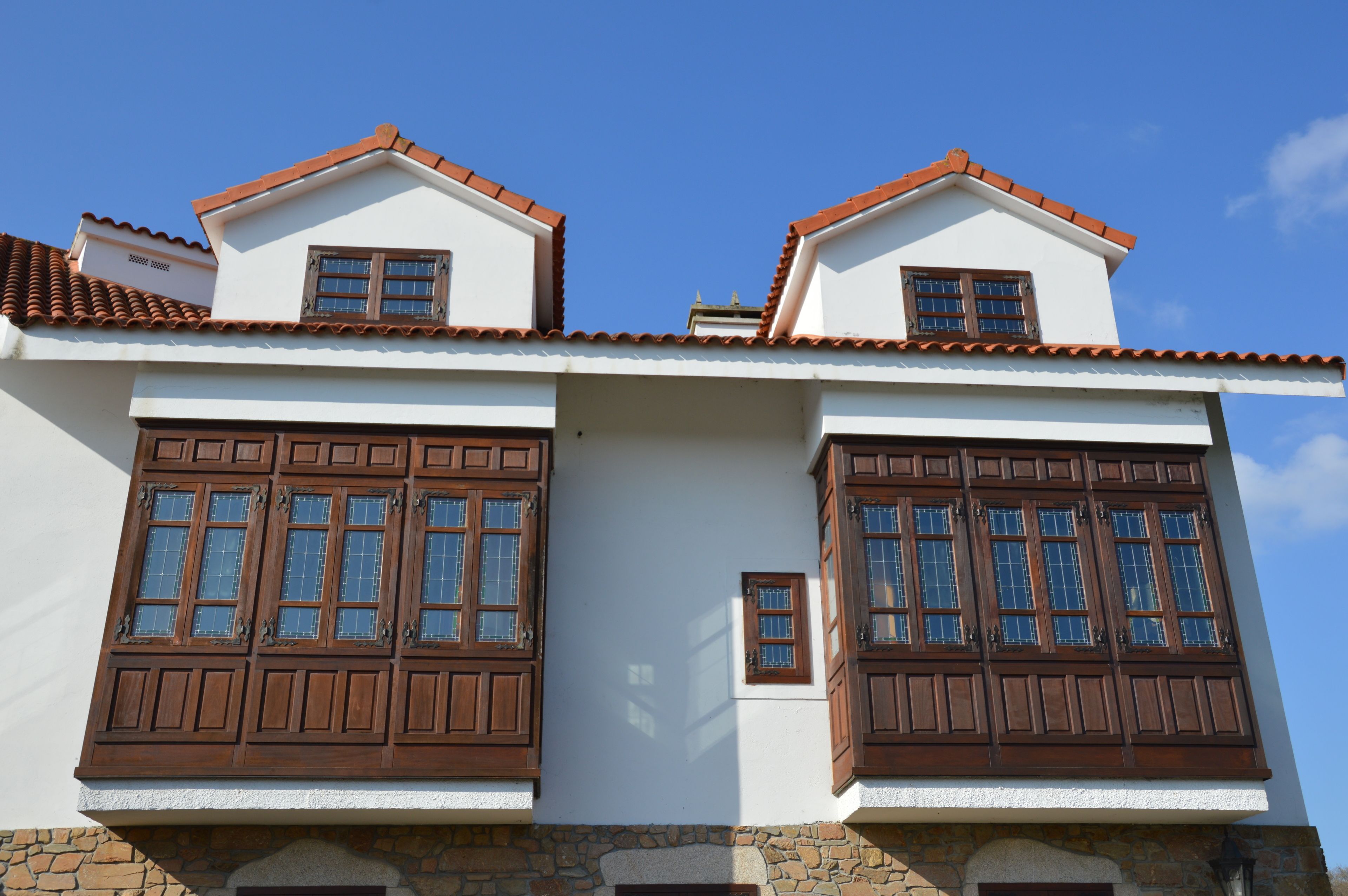 A two-story building with a white facade, brown wooden shutters, and a red-tiled roof.