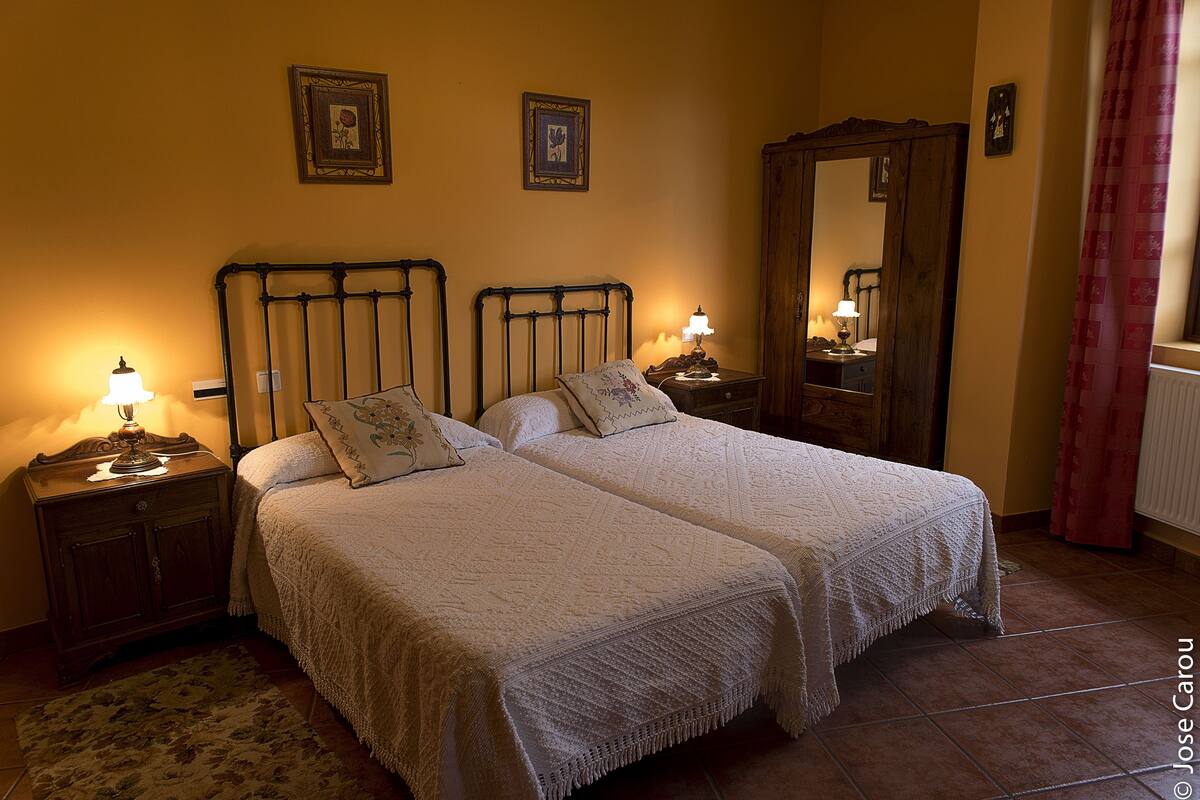 A double bed with a wooden headboard, two bedside tables with lamps, a mirror, and a floral rug.