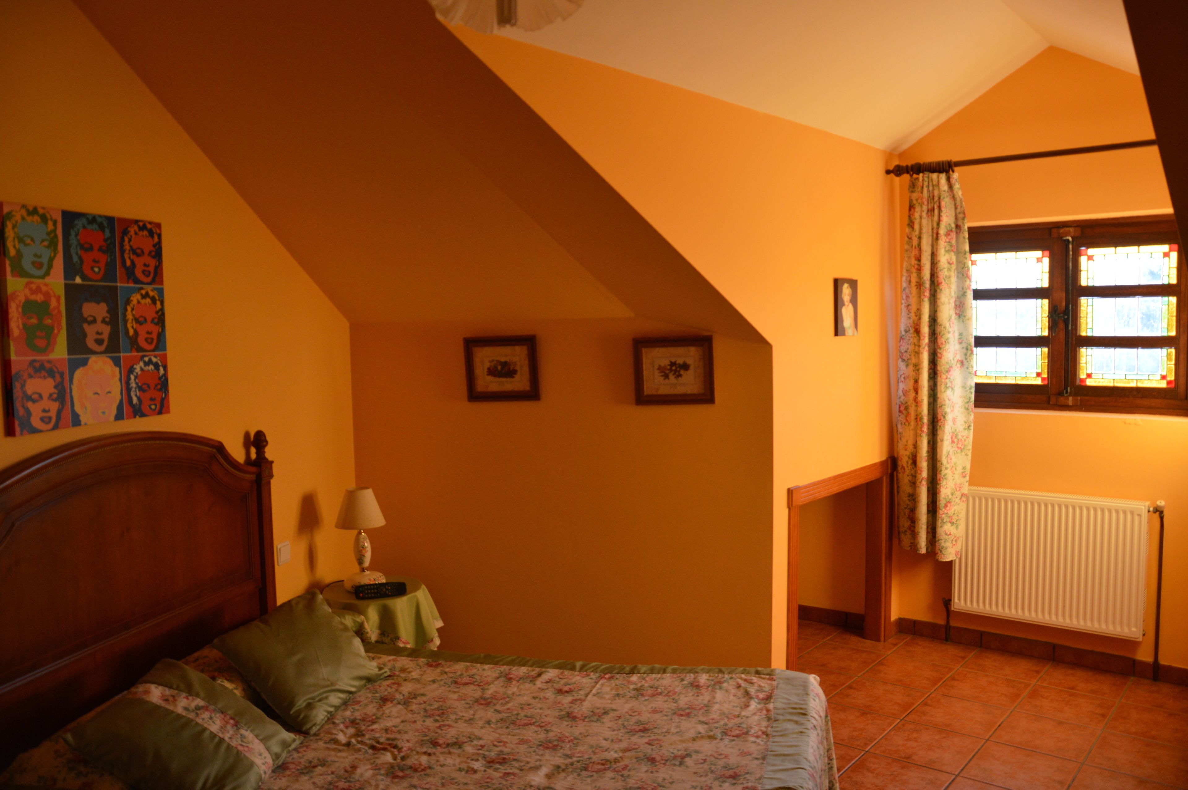 A bedroom with a sloped ceiling, a bed with floral bedding, a nightstand with a lamp, and a window with curtains.