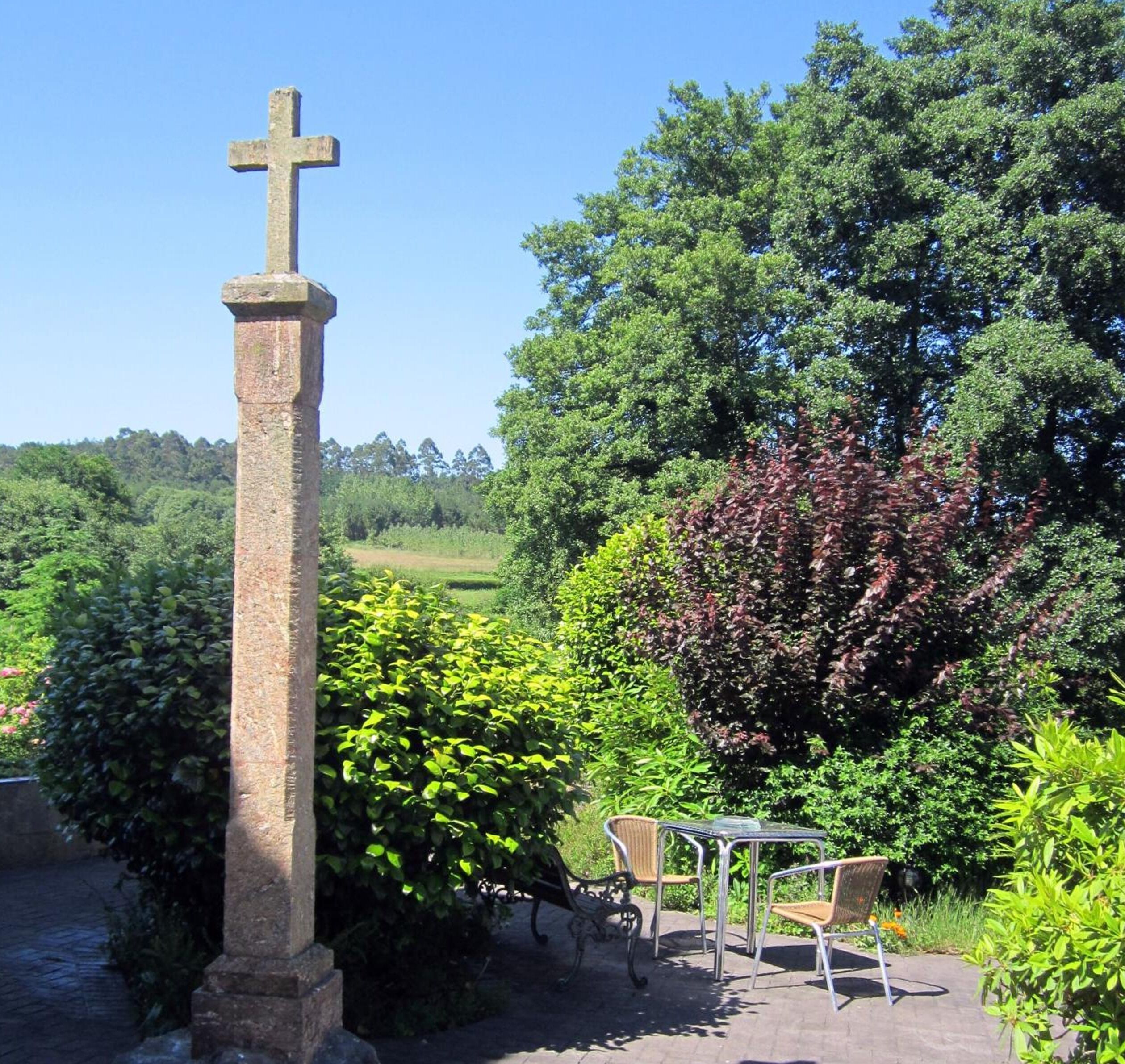 Ein Steinkreuz, ein gepflasterter Weg und ein Tisch mit Stühlen in einem Garten.