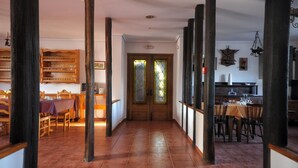 Un pasillo con pilares de madera, un comedor con mesa y sillas, y una cocina con mostrador y taburetes.