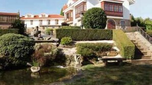 Un edificio grande y blanco con techo rojo, rodeado de jardines cuidados y un pequeño estanque.