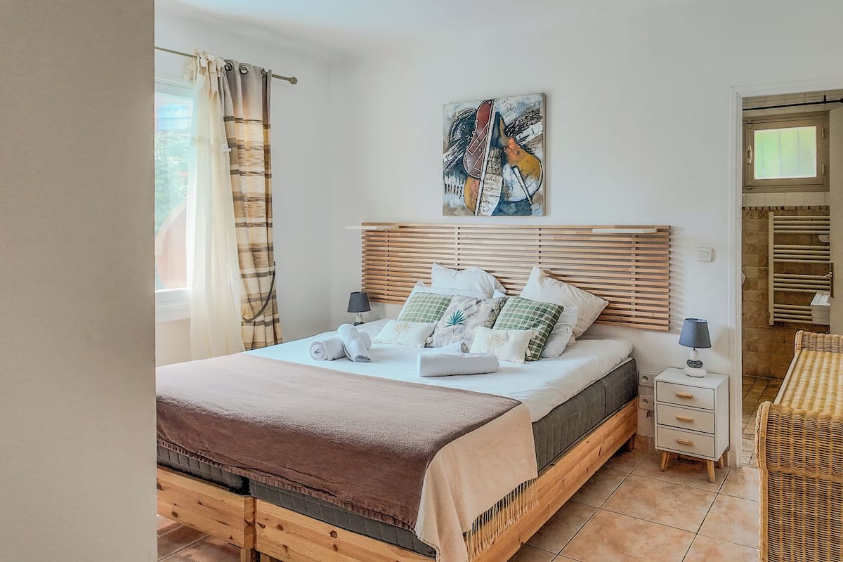 A bedroom with a bed, bedside tables, a lamp, a painting, and a wicker chair.