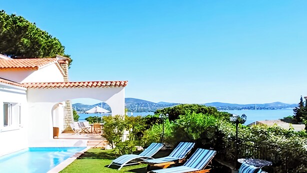 Un área junto a la piscina con sillones de descanso, una pérgola y vistas al mar y a las montañas.
