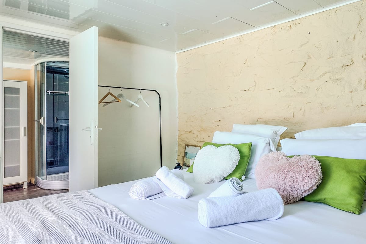 A hotel room with a bed, towels, pillows, a wardrobe, and a glass shower enclosure.