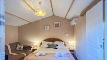 A bedroom with a large bed, a smaller sofa, a wooden ceiling, and a door.