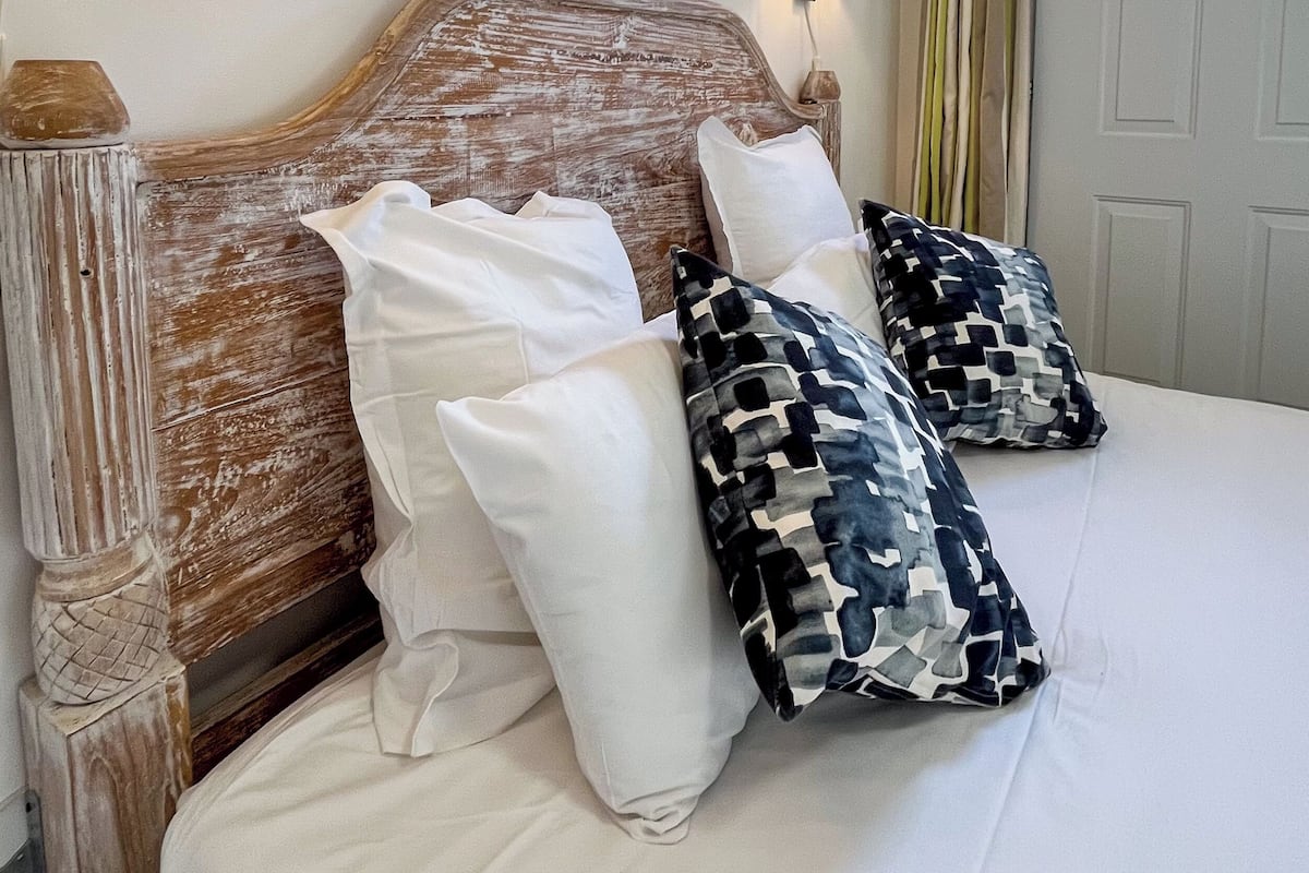 A neatly made bed with white and patterned pillows, a wooden headboard, and wall-mounted lamps.