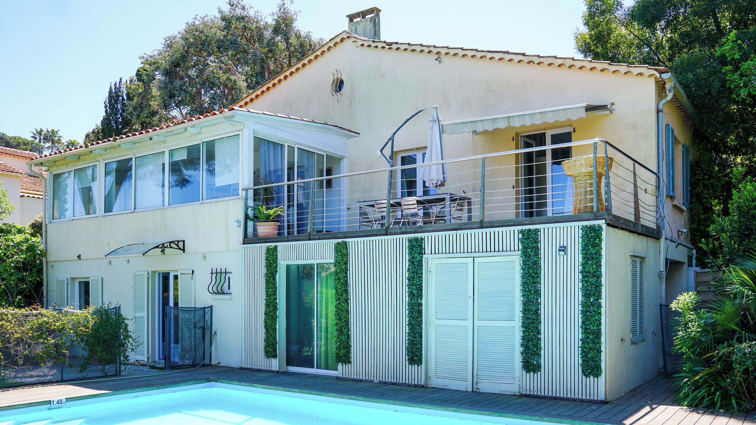 Ein zweigeschossiges Gebäude mit Swimmingpool, einem Balkon mit Gartenmöbeln und einem Garten.