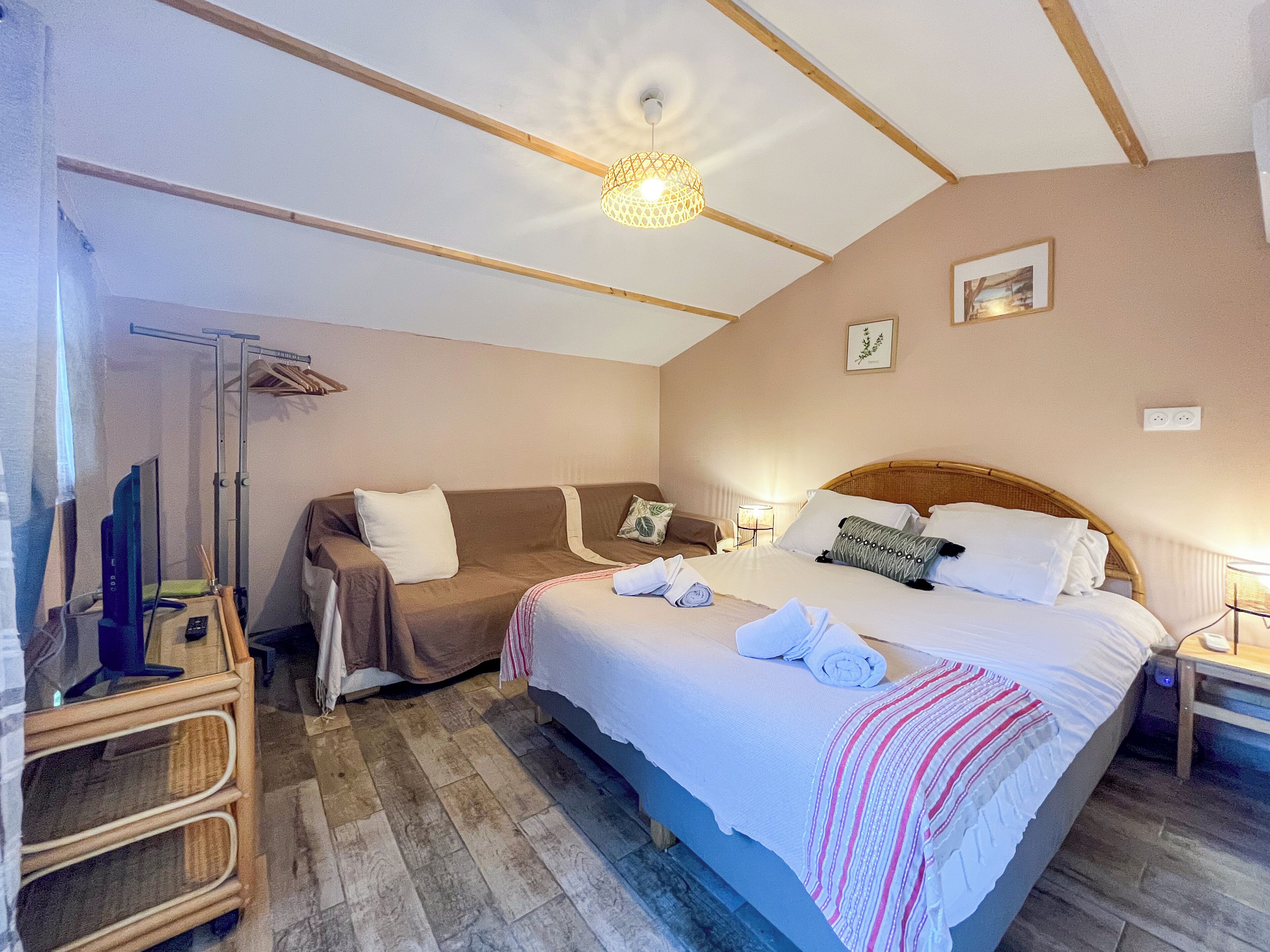 A hotel room with a bed, a sofa, a TV, and a desk with a lamp.