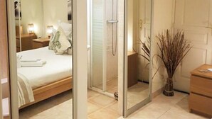 Un dormitorio moderno con cabina de ducha de vidrio, una cama con ropa blanca y una mesita de noche con lámpara.