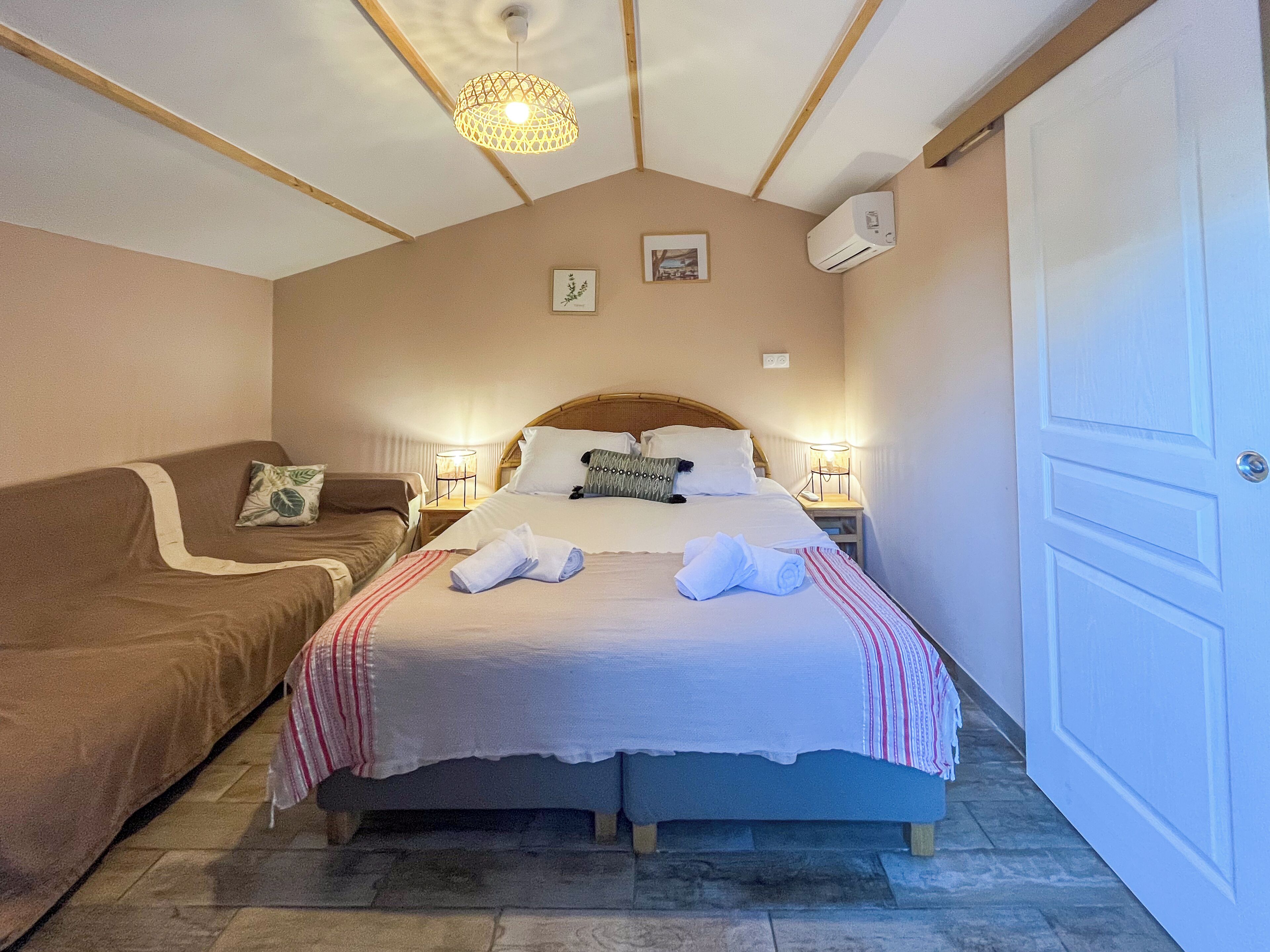 A bedroom with a double bed, a single bed, a sofa, and a door.