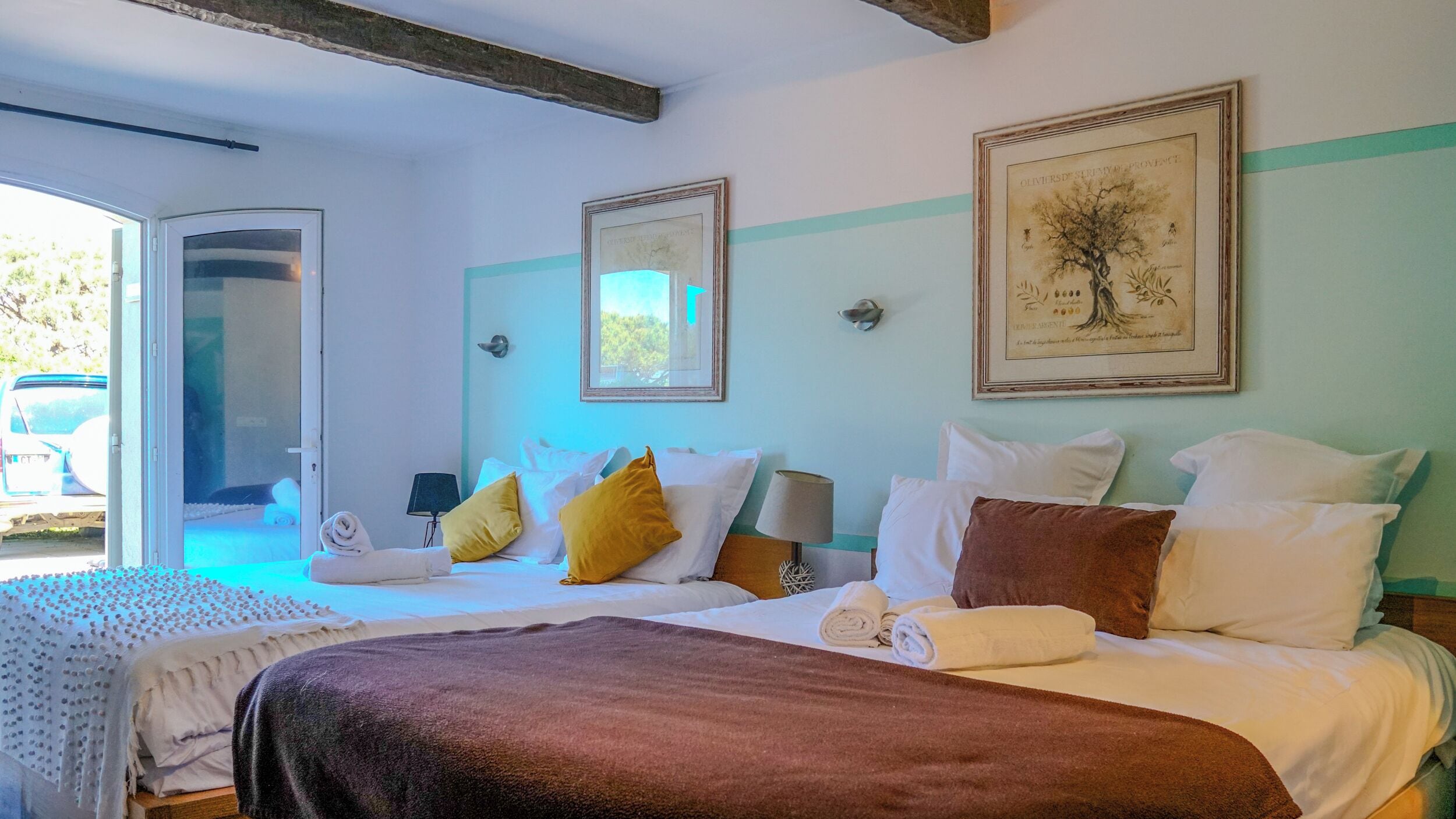 A hotel room with two beds, a large window, and a door leading outside.