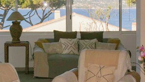 Un rincón acogedor con un sofá y sillones, una mesita con lámpara, y vistas a un cuerpo de agua y un paisaje lejano.