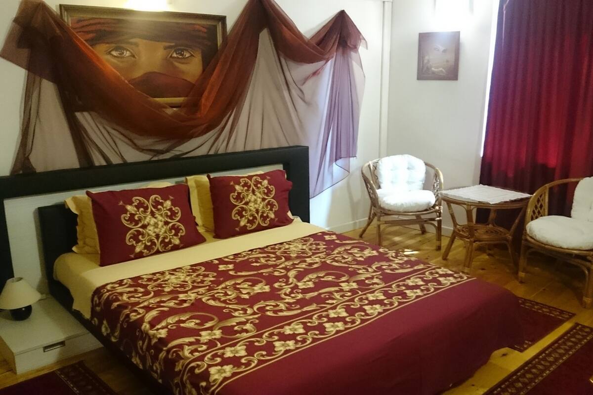 A bedroom with a large bed, a chair, a small table, and a painting on the wall.