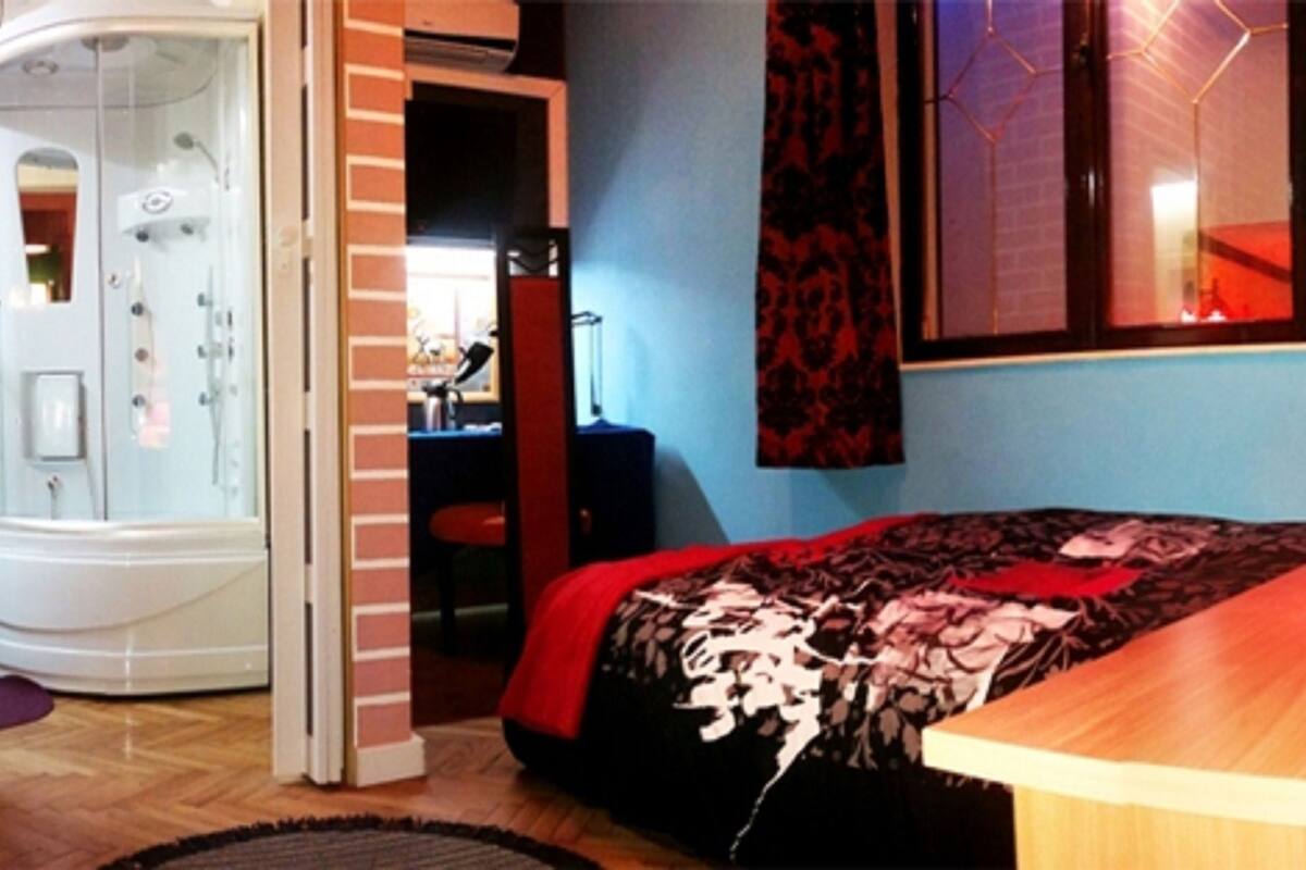A bedroom with a bed, a desk, a chair, a bathroom with a shower, and a wooden wardrobe.