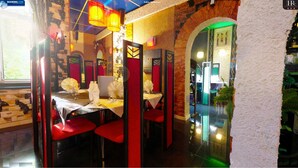Un restaurante con sillas rojas y manteles blancos, paredes de ladrillo y un arco iluminado en verde.