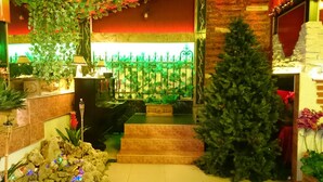 Una escalera conduce a una habitación con un árbol de Navidad, una pared decorada con follaje verde y una pared de piedra con una cortina roja.