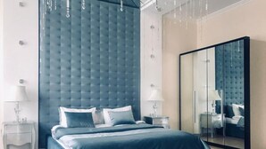 A modern bedroom with a tufted headboard, a large mirror, and a bed with blue bedding. - Dom Aktera (Odesa)