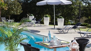 A poolside area with lounge chairs, a table with drinks, and umbrellas.