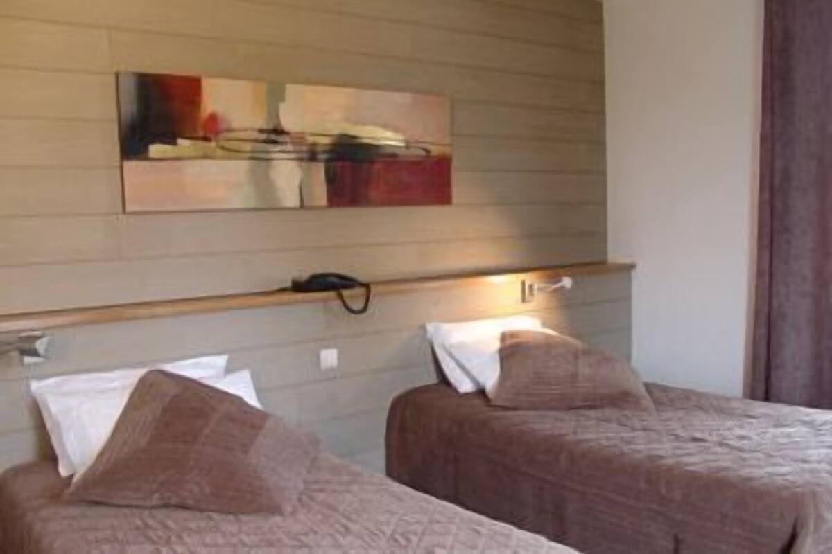 A hotel room with two beds, each with a pillow and a blanket. There is a wall-mounted artwork above the beds.