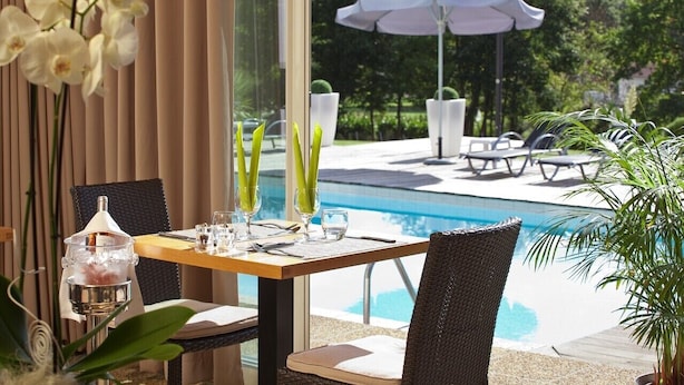 A dining table with a view of a swimming pool, outdoor seating, and a decorative orchid arrangement.