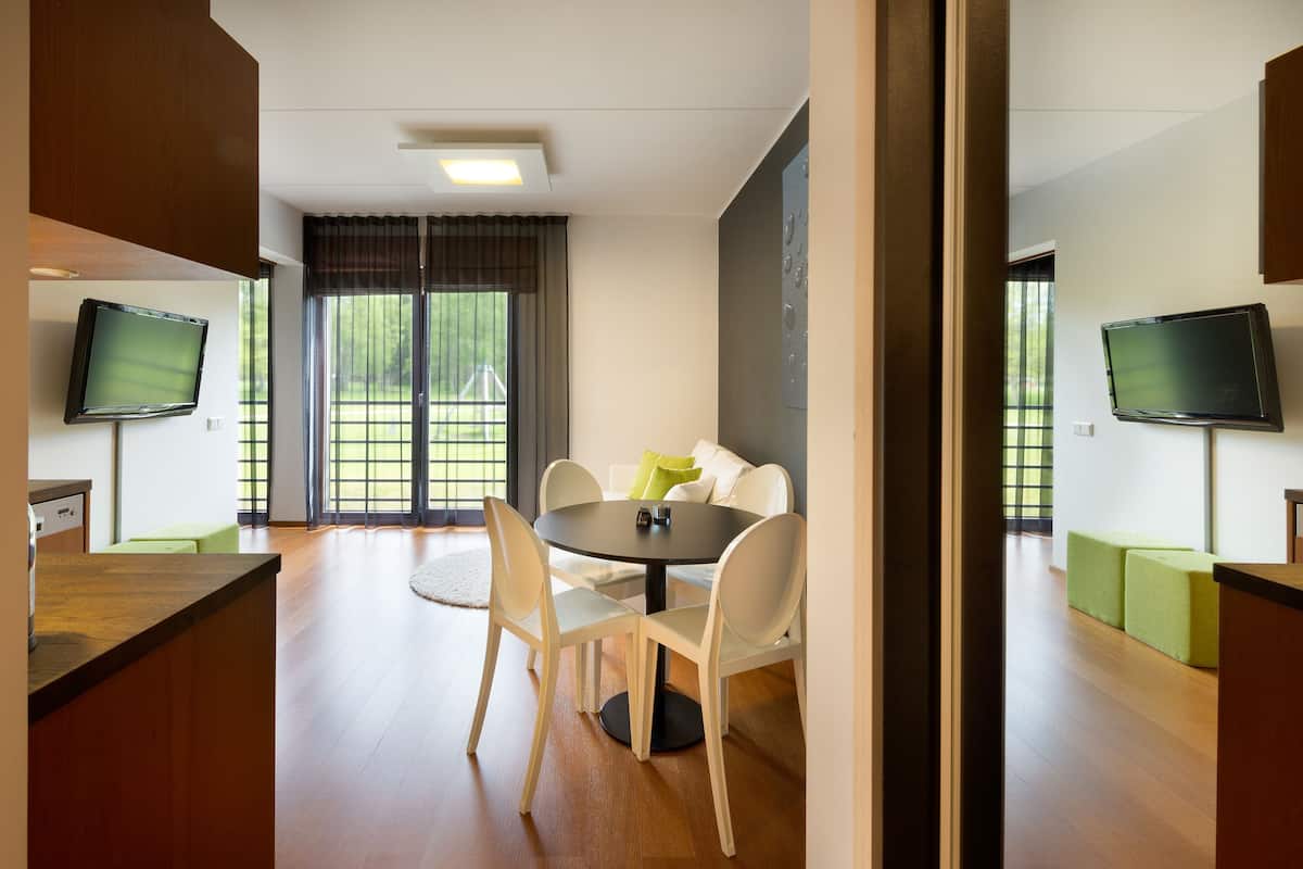 A modern dining area with a round table, white chairs, and a television on the wall.