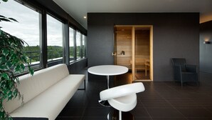 A modern interior with a white sofa, a round table, and a chair. There is a large window with a view of the outdoors. - GMP Clubhotel Apartments (Otepaa)