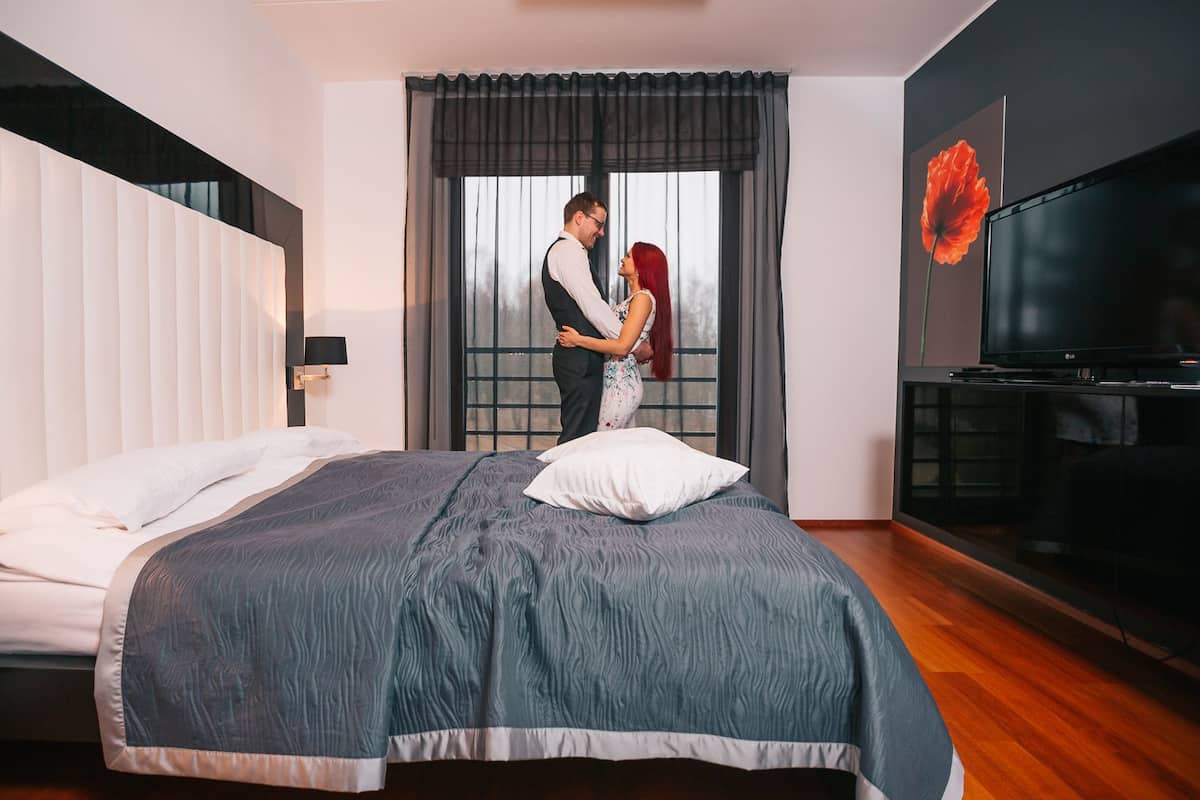 A modern hotel room with a large bed, a flat-screen TV, and a large window with curtains.