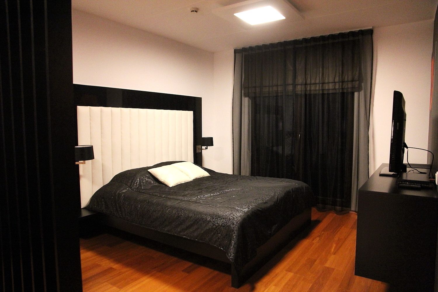 Habitación de hotel con cama, escritorio con computadora y ventana con cortinas.