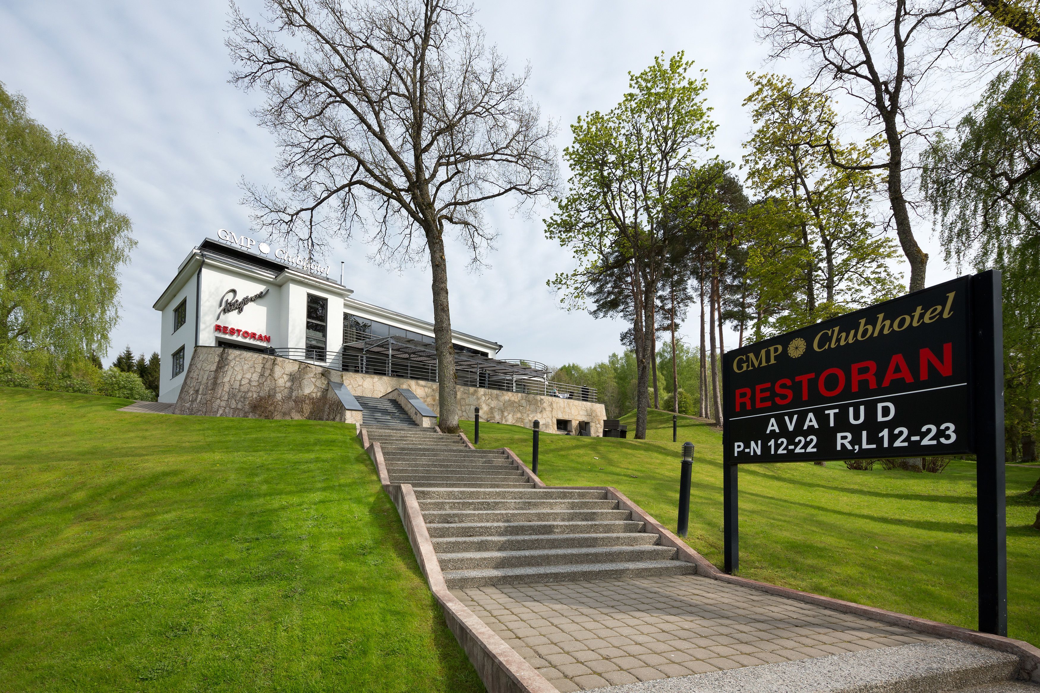 A building labeled 'Restoran' with a staircase leading up to it, surrounded by trees and grass.