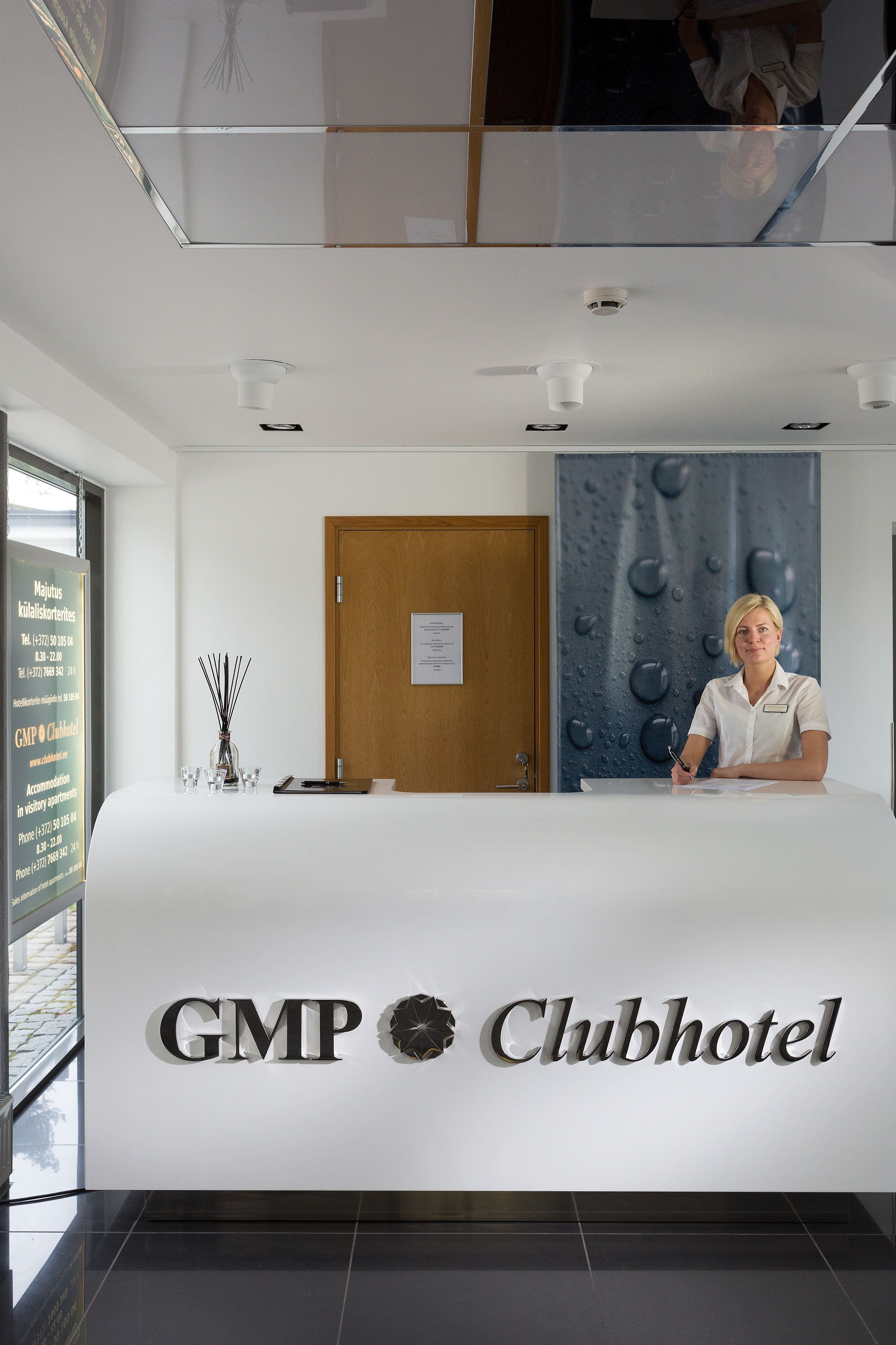 Een receptiebalie bij het GMP Clubhotel, met een receptionist, een houten deur en een muur met een ontwerp van een waterdruppel.