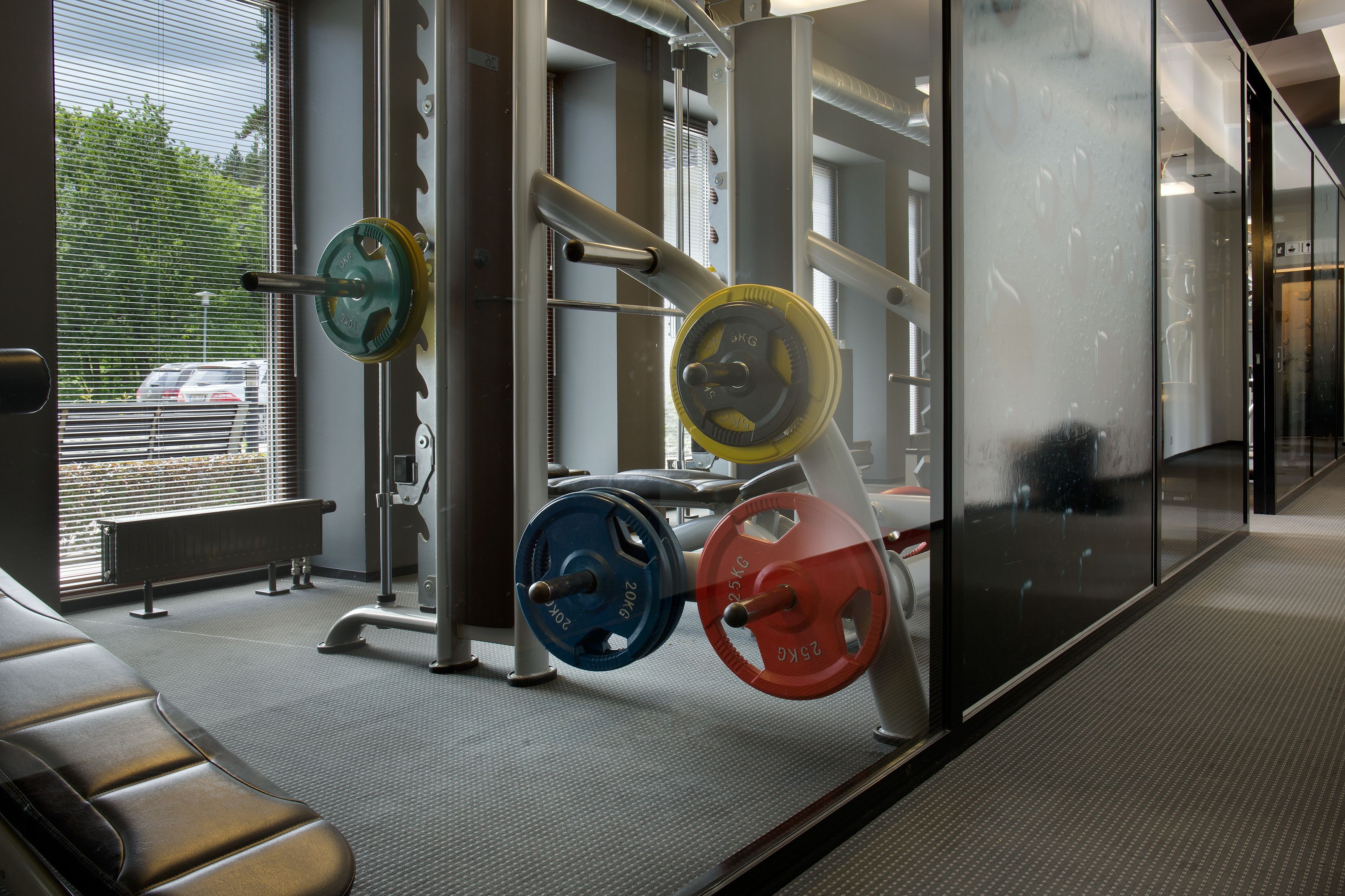 Un gimnasio con equipamiento de levantamiento de pesas, una banca y vista a un coche por la ventana.
