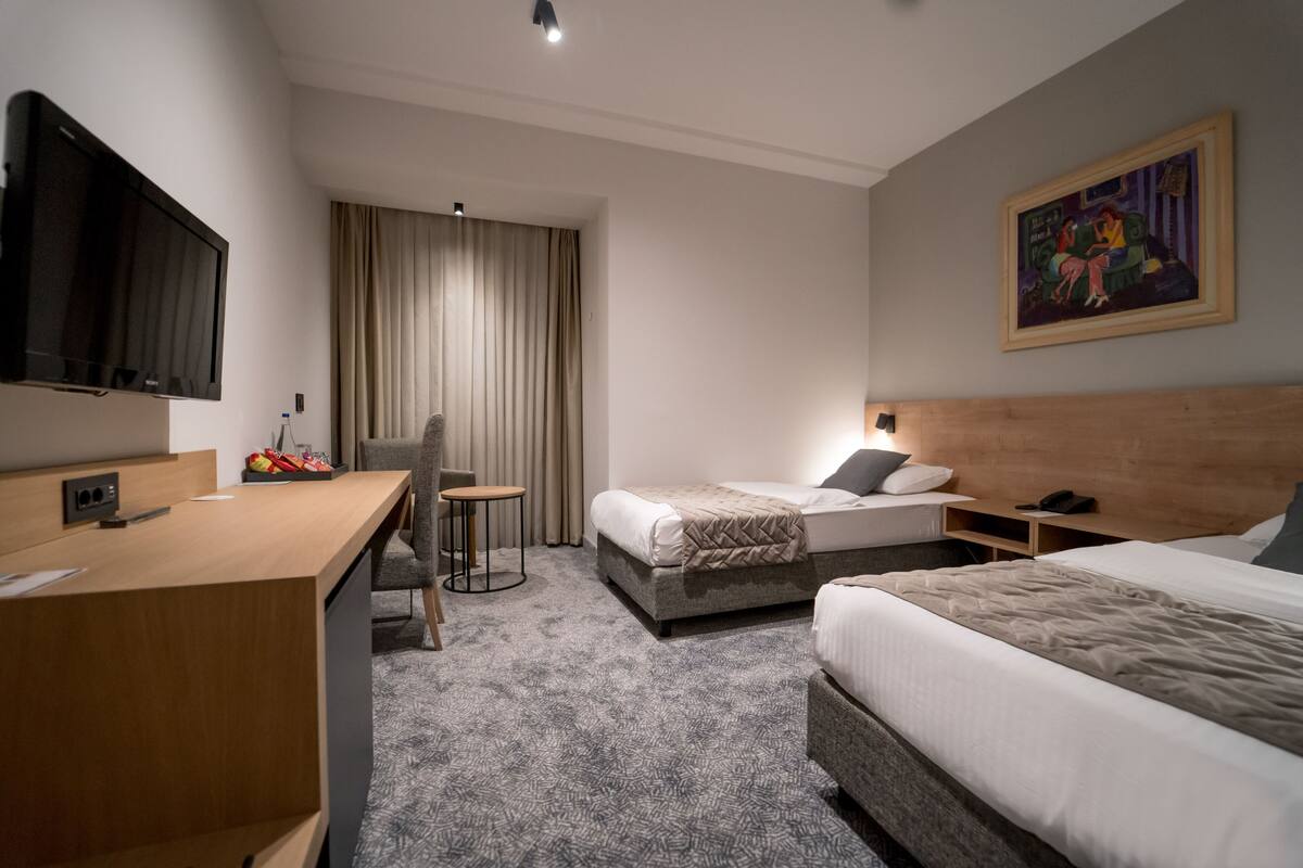 A hotel room with a bed, a desk, a chair, a television, and a painting on the wall.