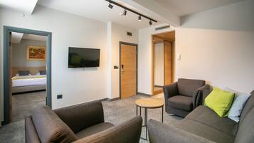 Una habitación de hotel moderna con una cama grande, un televisor de pantalla plana, dos sofás, una mesa redonda pequeña y una puerta de madera.