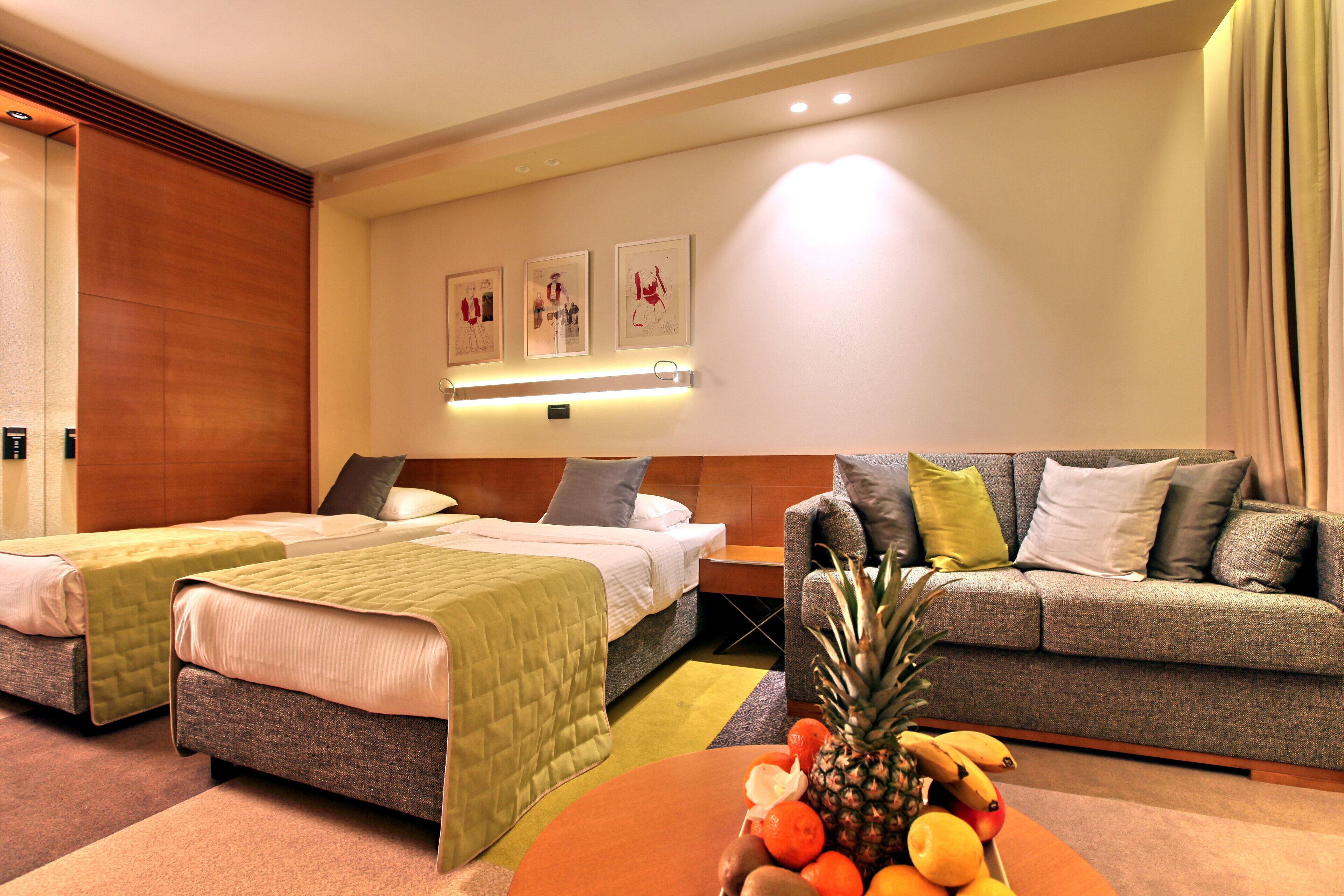 Habitación de hotel con dos camas, un sofá, un frutero y obras de arte en la pared.