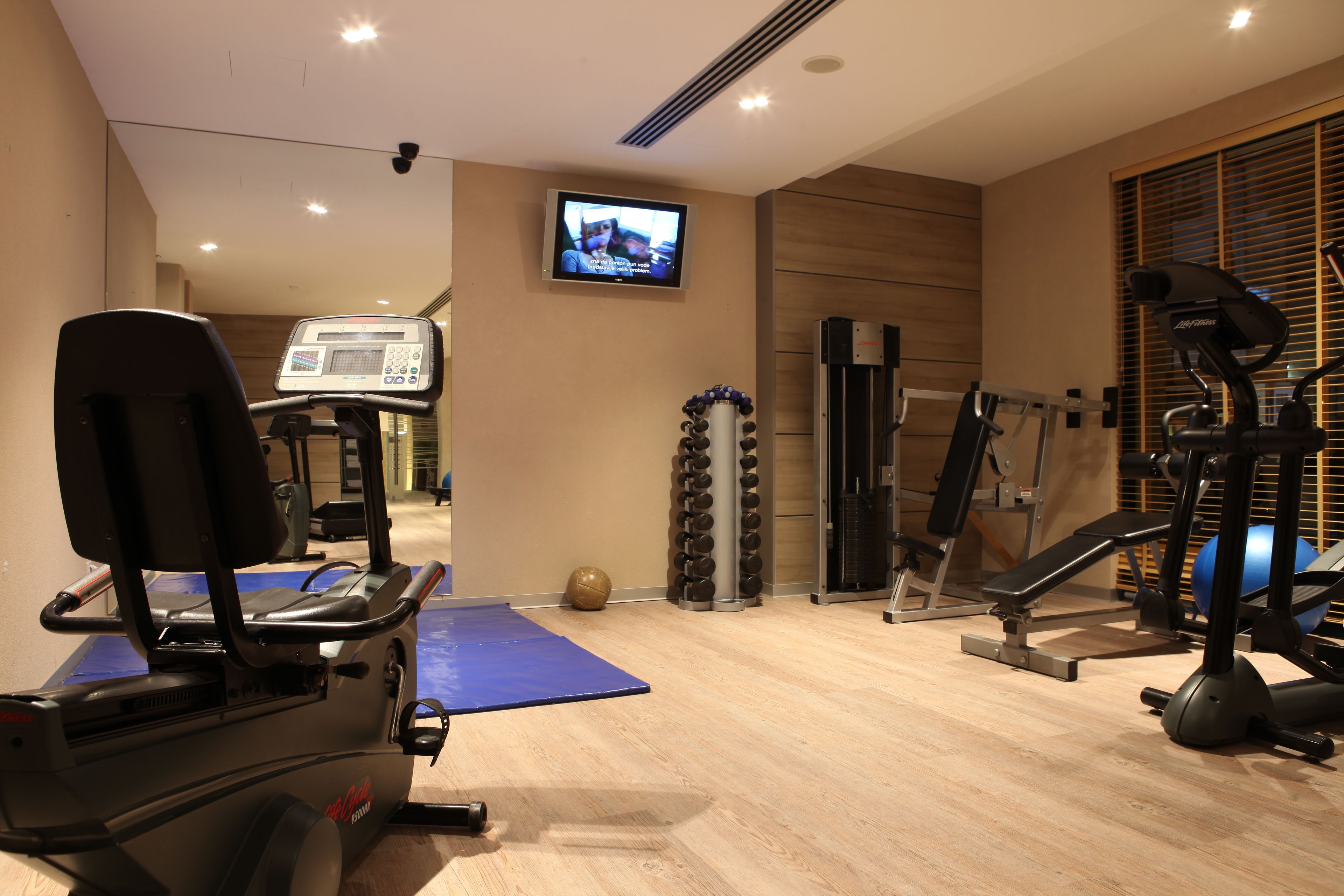 A gym with exercise equipment, a treadmill, and a television screen.